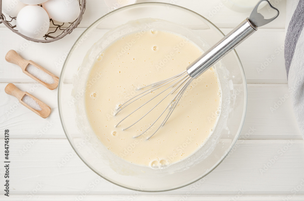 Cooking dough for traditional thin pancakes or crepes. Eggs, flour, salt, sugar, milk and butter in a bowl on a white wooden background. Recipe step by step. Food for Maslenitsa. Cooking dough for traditional thin pancakes or crepes. Eggs, flour, salt, sugar, milk and butter in a bowl on a white wooden background. Recipe step by step. Food for Maslenitsa.