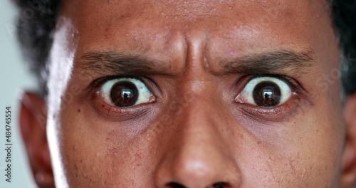 Surprised African descent close-up eyes reaction, looking to camera. Back person eye SHOCK