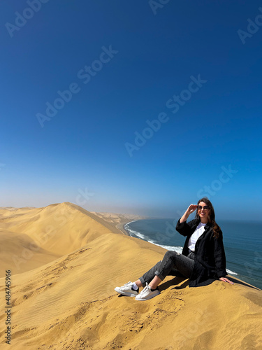 A young woman sitting at sandy dunes on seashore. Sandwich Harbour in Namibia.