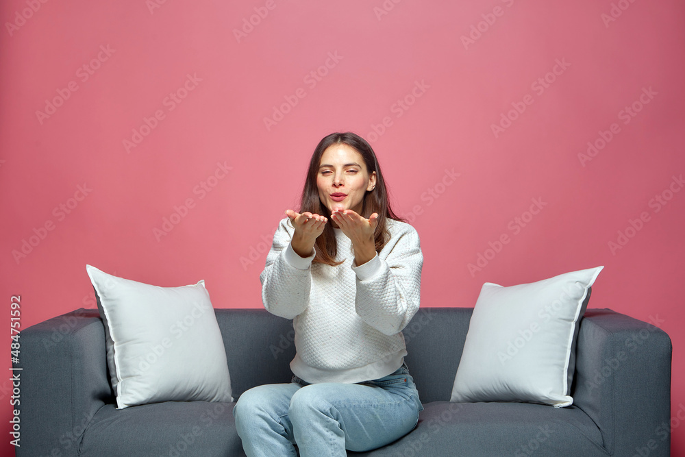 Happy young girl blogger send blow kiss looking at camera showing love, gratitude and affection, sitting on sofa