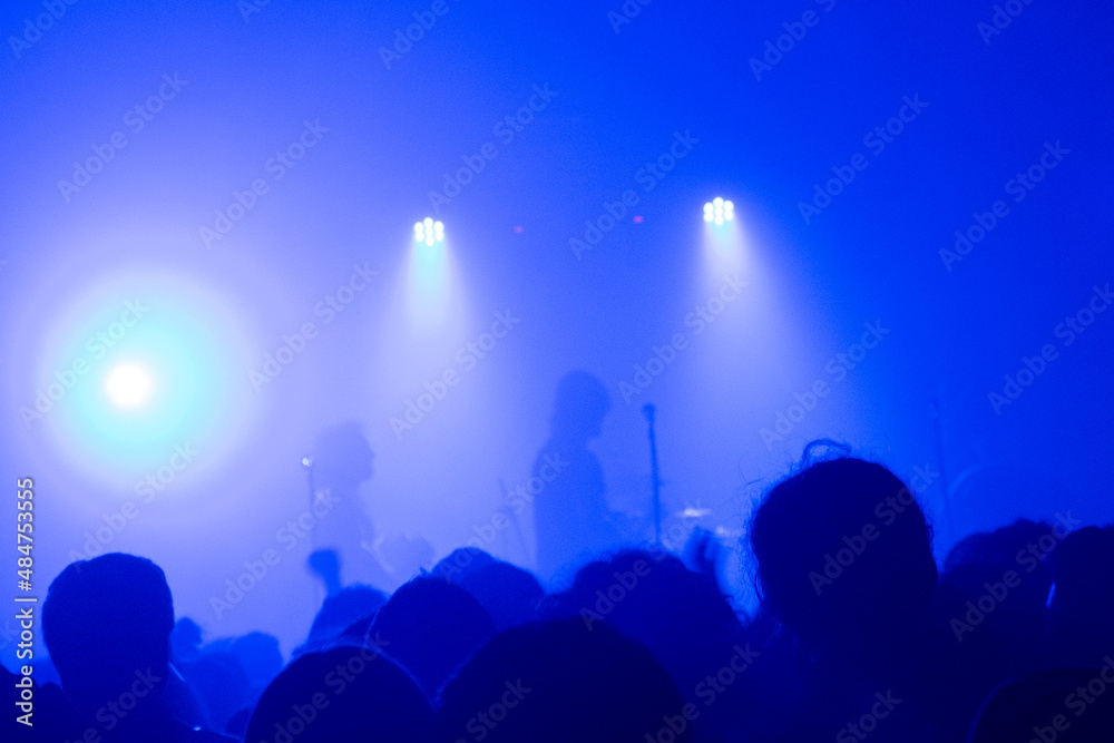 Grupo tocando en directo, cabezas de público, predomina luz azul.