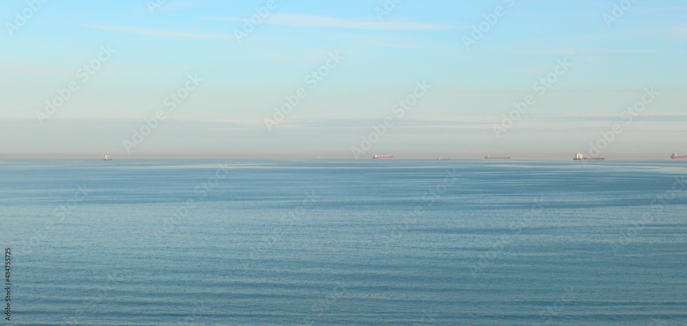 Seascape, blue sea, calm, horizon line, and ships in the roadstead in the distance