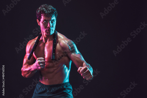 Half length of strong male athlete who poses with nunchaku on black background. Sport concept  photo