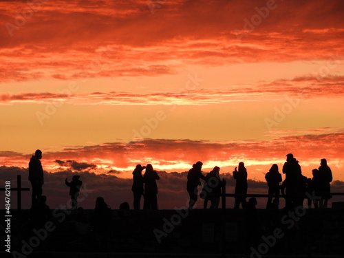 Dark silhouette of people watching the sunset over the sea on the horizon
