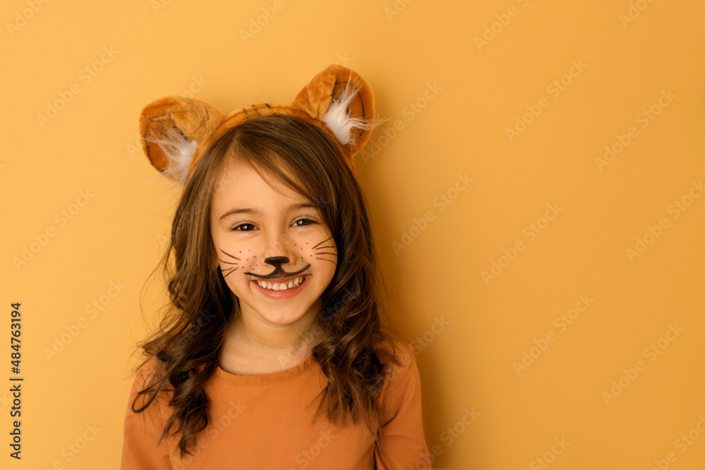 Laughing child with painted moustaches, with ears in the guise of a tiger. A girl dressed up in the symbol of the new year 2022 according to the Chinese zodiac