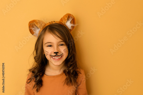 Laughing child with painted moustaches, with ears in the guise of a tiger. A girl dressed up in the symbol of the new year 2022 according to the Chinese zodiac