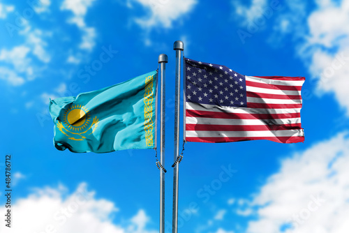 Flags of Kazakhstan and America on the wind against blue sky