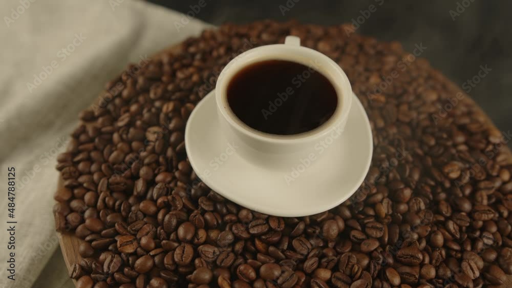 Cup of coffee and saucer on coffee beans with dissipating steam. Composition of freshly brewed coffee on roasted beans with smoke. Concept of preparation fragrant drink. Cup of coffee and saucer on coffee beans with dissipating steam. Composition of freshly brewed coffee on roasted beans with smoke. Concept of preparation fragrant drink.