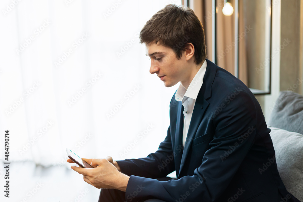 caucasian businessman working with mobile phone, wear suit, sit on sofa, copy space with window light. Young man work business with home office background and copy space caucasian businessman working with mobile phone, wear suit, sit on sofa, copy space with window light. Young man work business with home office background and copy space