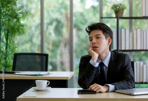 Young asian employee sit with absent-minded in the office on a table with tablet, laptop computer and a cup of coffee.