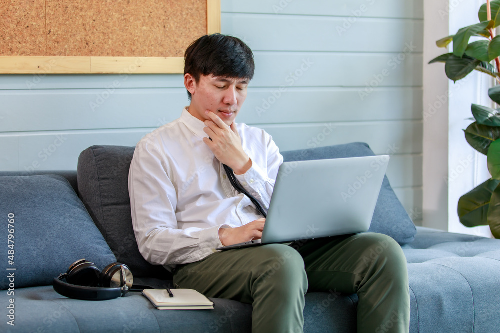 Young businessman working with laptop on resting couch of office lobby and close eyes to think solution about marketing strategy and planning network to solve difficult task. Young businessman working with laptop on resting couch of office lobby and close eyes to think solution about marketing strategy and planning network to solve difficult task.