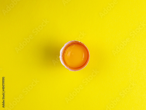 one broken brown chicken egg and egg yolk on the bright sunny yellow background. Top view from above, copy space, trend minimalism