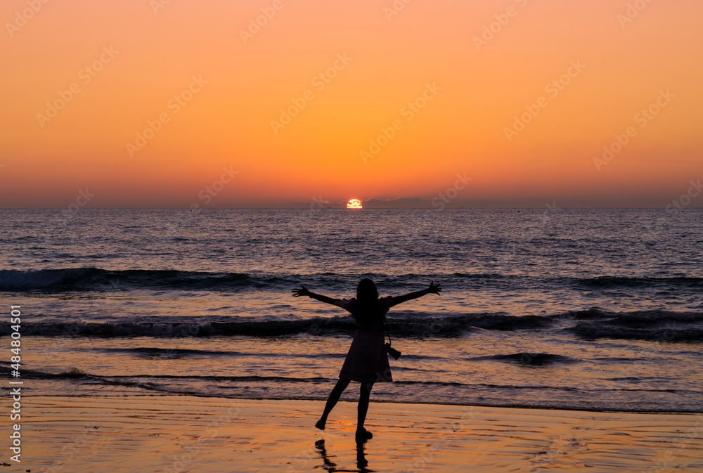 landscape of sunset sunset on sea at Khaolak beach with defocused silhouette happy woman standing looking at view freedom raise hands. orange sky. travel attraction in Phangnga, Thailand.