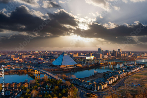 a stunning aerial shot of the the skyscrapers and office buildings in the cityscape along Wolf River Harbor with a glass pyramid and powerful clouds at sunset at Greenbelt Park on Mud Island