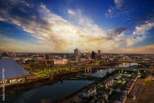 A stunning aerial shot of the skyscrapers, lights and buildings in the cityscape along the Mississippi river at sunset with blue sky and powerful clouds at Greenbelt Park on Mud Island in Memphis