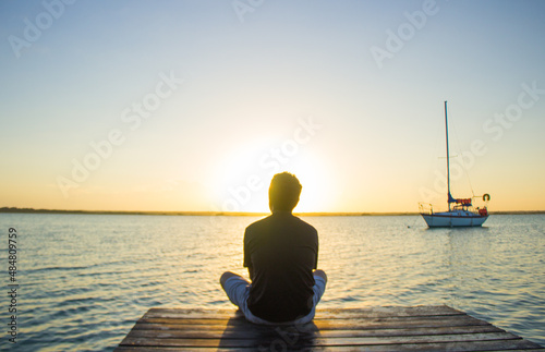 Hermosa imagen de un chico viendo el amanecer a la orilla de un muelle