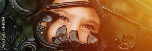 portrait happy candid eight year old caucasian kid girl brown eyes peeking through of abstract metal shapes in nature. prepubertal age of children, mind psychology and mental health. banner. flare photo