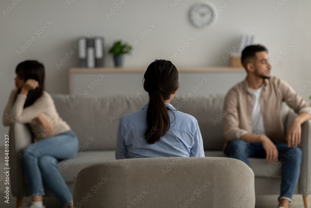 Back view of female psychologist giving therapy session to quarreling arab couple at office, helping them with conflict Back view of female psychologist giving therapy session to quarreling arab couple at office, helping them with conflict