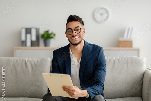 Wallpaper Mural Portrait of happy arab male psychologist smiling at camera and taking notes duri