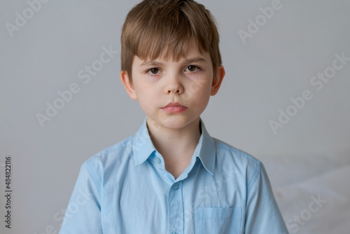 A small caucasian boy in casual blue shirt looks into camera with serious look, natural expression. Confident look straight with brown eyes