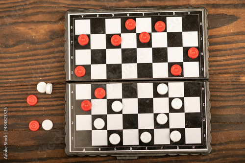 A board for playing checkers with chips on a wooden table, close-up, selective focus.