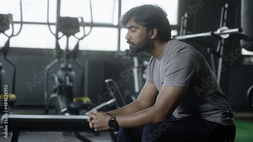 Young Indian athlete thinking or resting at gym after wrokout - Concept of thoughtful, relaxation and fitness center.