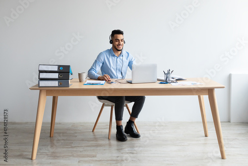 Arab man using laptop wearing headset sitting at desk