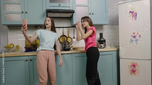 Two girl bloggers filming video content on phone for their blogs or social networks. Creation trend content in kitchen for media account or vlog. Slow motion ready, 4K at 59.97fps. photo