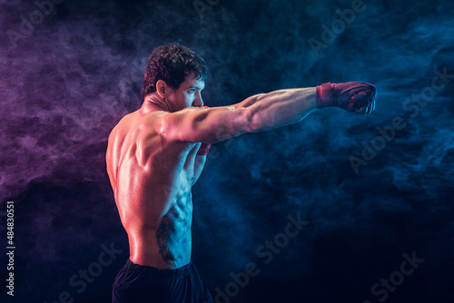 Side view of aggressive boxer who training and practicing jab on smoke background. Sport concept