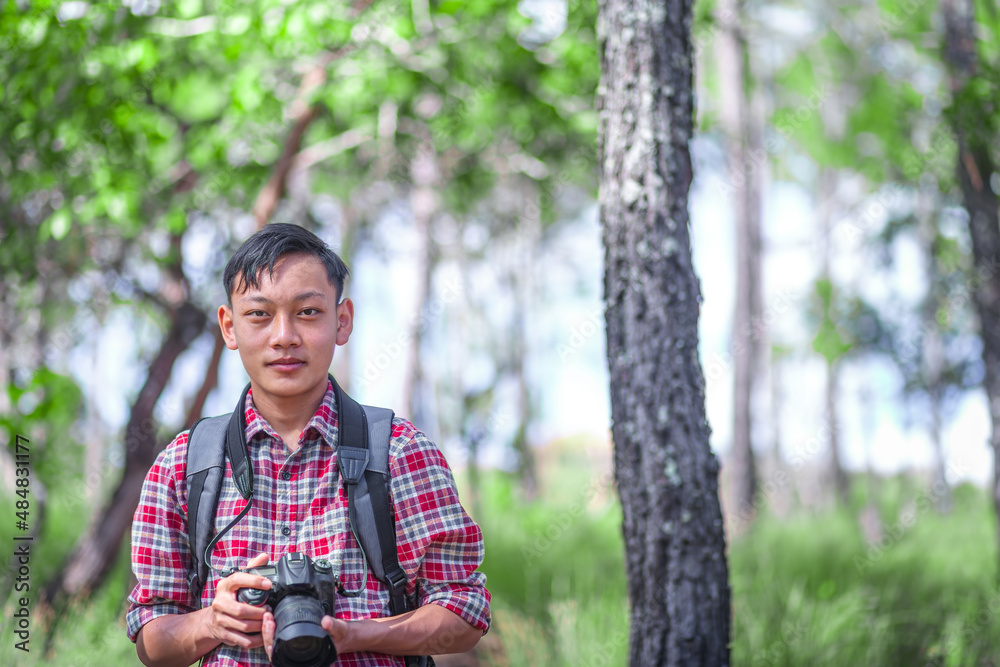 Happy young man holding a camera while standing at the forest. Environmental studies.