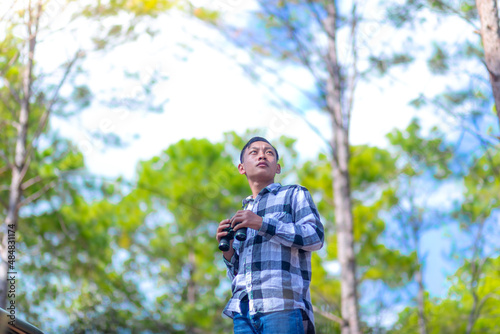 Young man uses binoculars while standing at the forest. Environmental studies. © surachat