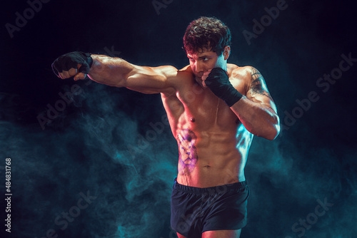 Half length of muscular boxer who training and practicing jab on smoke background. Sport concept