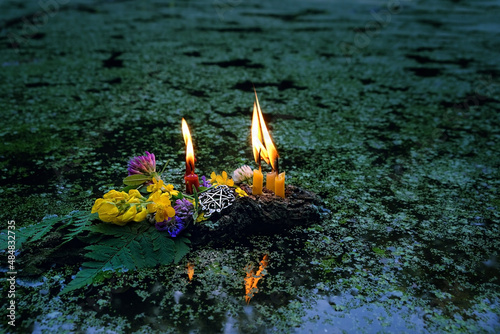 flowers, pentagram amulet, burning candles on dark water, covered aquatic plants duckweeds (Lemna). old tradition, fortune telling for pagan holiday. Summer Solstice Day, Midsummer, Litha sabbat