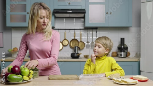 Young woman and boy prepare healthy snack and put it in lunchbox. Mom and son filming stories for social media cooking blog. Family bloggers, culinary account. Slow motion ready, 4K at 59.97fps. photo