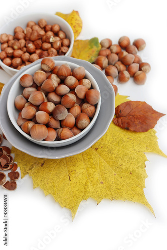 Whole hazenuts in a bowl with cracked hazenuts and autumnal leaves on white background photo