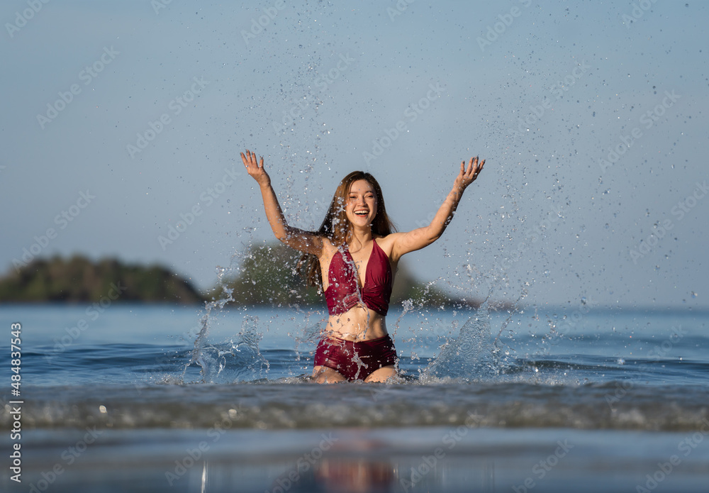 cheerful woman in swimsuit playing water splashing on the sea beach at Koh Chang island, Thailand