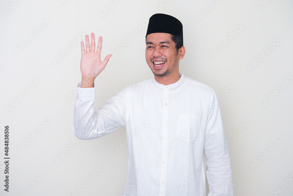 Moslem Asian man showing happy expression when waving hand to greet someone Moslem Asian man showing happy expression when waving hand to greet someone