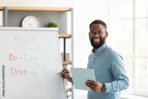Fotografie Smiling millennial african american bearded guy teacher in glasses stands near b