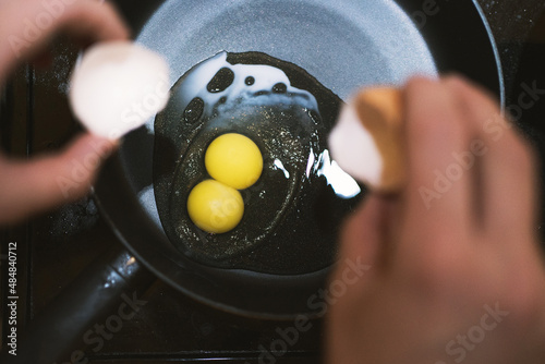 The shell of one egg in female hands over a frying pan with one egg and two yolks.