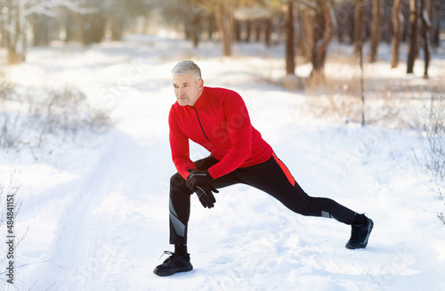 Healthy lifestyle. Full length of mature man in sportswear stretching legs before running outdoors on snowy winter day © Prostock-studio