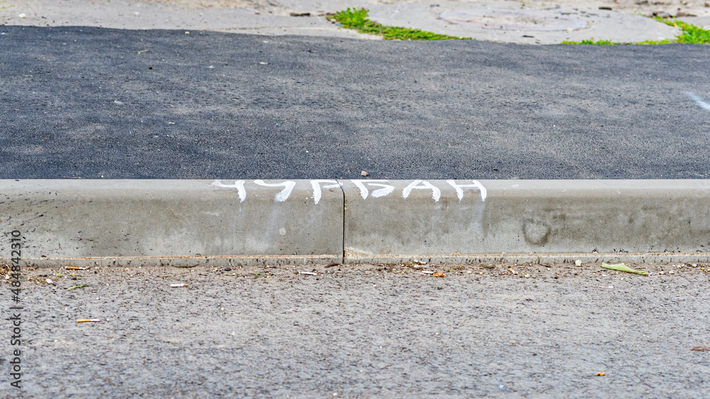 Curb stone on the asphalt road. Translation of the inscription: block of wood