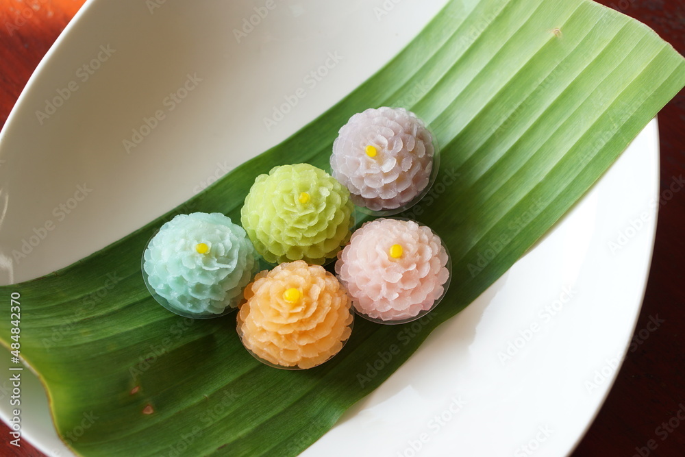 Top view of Thai dessert flower shape stuff with crushed soybean and taro on wood table with banana leaf and white dish. (Thai name is Khanom Chor Phaka Krong) Top view of Thai dessert flower shape stuff with crushed soybean and taro on wood table with banana leaf and white dish. (Thai name is Khanom Chor Phaka Krong)