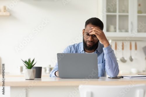 Sad tired unhappy depressed millennial african american bearded male in glasses working on laptop