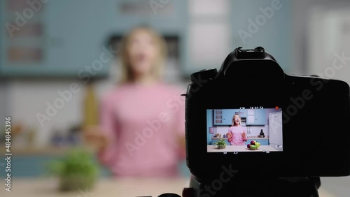 Young woman talks to camera about benefits of fruits, vitamins and healthy diet. Female blogger filming stories in kitchen for social media cooking blog. Slow motion ready, 4K at 59.97fps. photo