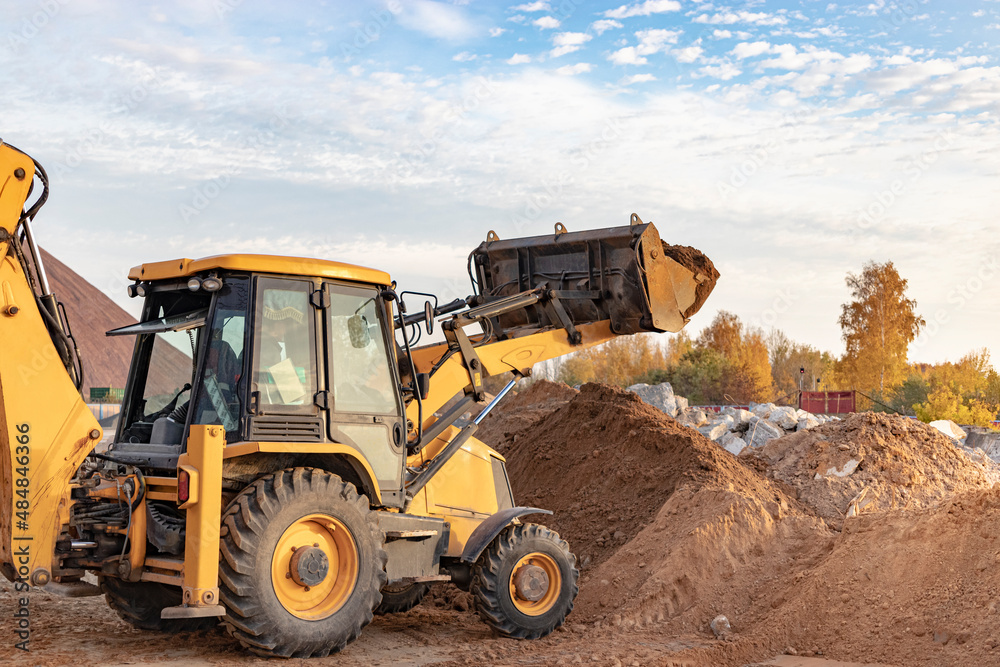 The excavator loader works with a bucket for transporting sand at a construction site. Professional construction equipment for earthworks. The excavator loader works with a bucket for transporting sand at a construction site. Professional construction equipment for earthworks.