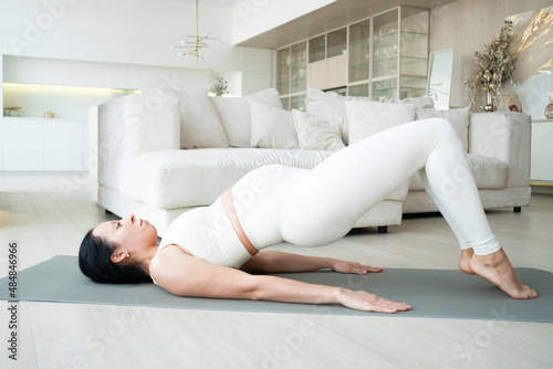 A pregnant woman in the living room at home is doing a twine exercise. Fitness during pregnancy.