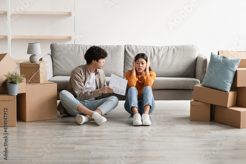 Unhappy Asian couple having argument over house rental or purchase documents in their new apartment on moving day