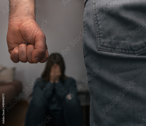 Man raises his fist to mistreat a helpless woman, sitting on the ground, covering her face with her hands, frightened