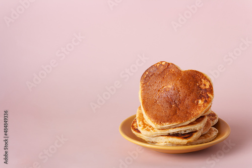 heart shaped pancakes lie in a yellow plate on a beige background, copy space photo