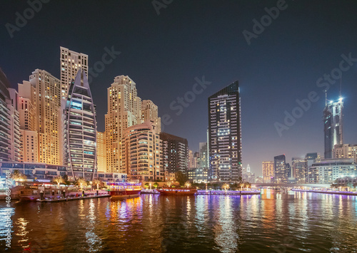 Dubai Marina Port, UAE, United Arab Emirates - Night view of high-rise buildings of residential district in Dubai Marina And Tourist Boat, Sightseeing Boat Sailing On Dubai Marina. © Grigory Bruev